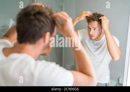 Hair loss man looking in bathroom mirror putting wax touching his hair styling or checking for hair loss problem. Male problem of losing hairs Stock Photo