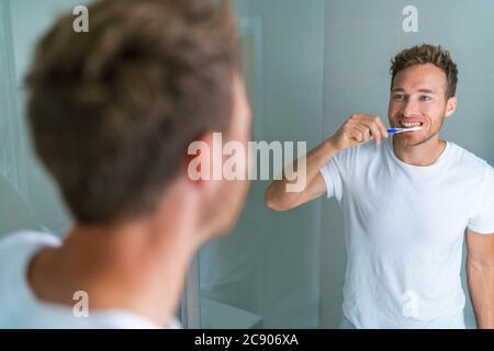 Brushing teeth man looking in mirror of home bathroom using toothbrush in morning routine for clean dental oral care Stock Photo