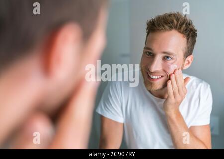 Handsome young man putting facial treatment face cream on clean skin in the morning after wash for skin moisturizing care. Dry skin problem. Men Stock Photo