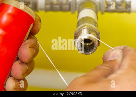 Worker installing sealing tape for water pipe fitting.Plumber putting seal tape on a thread of a plumbing fitting. Stock Photo