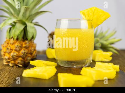 A glass of pineapple juice with pineapple slice on wooden table background. Stock Photo