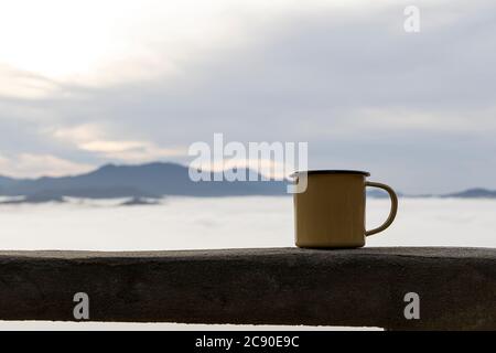 Close up a yellow tin cup of hot coffee with  fog on the mountain background in the morning. Stock Photo