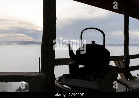 Close up of old kettle with charcoal stove and fog on the mountain background in the morning. Stock Photo