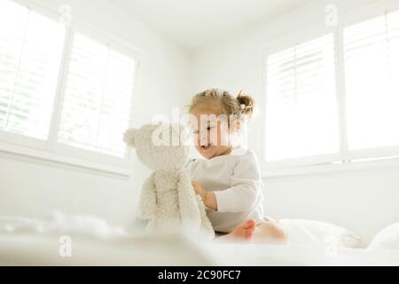 Toddler girl playing on bed with her teddy bear toy Stock Photo