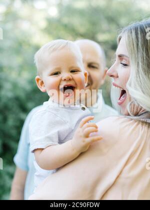 Baby boy laughing outdoors with his parents