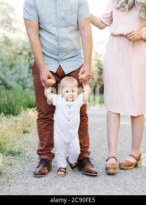 Parents assisting baby son learning to walk outdoors Stock Photo