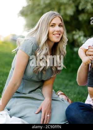 Outdoor portrait of smiling woman sitting o grass with her family nearby Stock Photo