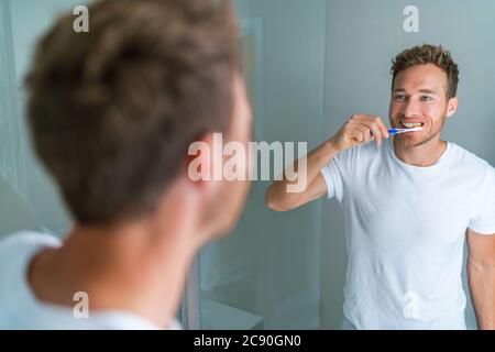 Brushing teeth man looking in mirror of home bathroom using toothbrush in morning routine for clean dental oral care Stock Photo