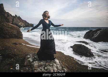 Ukraine, Crimea, Young woman standing on rocky beach Stock Photo