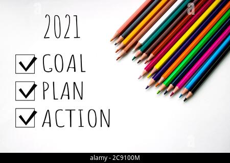 Multi-colored sharpened pencils on a white background with the inscription 2021, goal, plan, action. Copy space. Rainbow pencils lie in the lower rugh Stock Photo