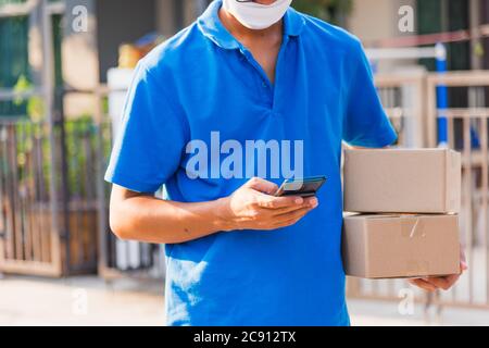 Asian delivery man courier online holding deliveries out boxes and using mobile phone contact the customer he protective face mask service under curfe Stock Photo