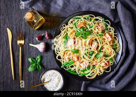 Italian spaghetti with green bean and salmon, decorated with basil leaves, served on a black plate on a dark wooden background with mustard seed sauce Stock Photo