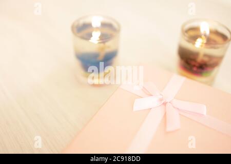 A gift box for a special occasion wrapped in pink paper and placed on a table near a gel candle. Stock Photo