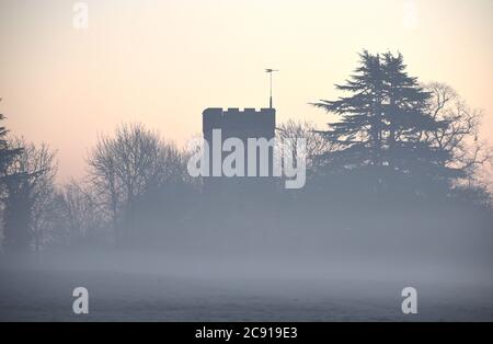 Mist lies in a frosty meadow in front of a church in this photo taken on a cold morning in December Stock Photo