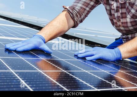 Male worker hands in glows on solar panel, technician installing solar panels on roof. Alternative energy sun energy power, ecological concept. Stock Photo