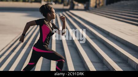 Morning running. African american girl with wireless headphones and fitness tracker runs up the stairs Stock Photo