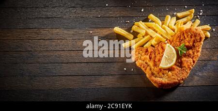 Schnitzel with French fries seasoned with salt and spices and served with lemon on a rustic wooden table with copyspace viewed from the top down in a Stock Photo