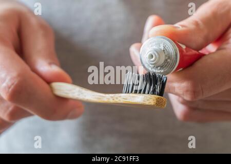 Male hands applying toothpaste on eco natural bamboo toothbrush. Zero waste home, plastic free items Stock Photo