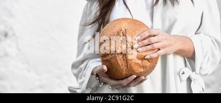 Woman holding a freshly baked round loaf of bread with the crust towards the camera in a close up on her hands with copy space in a panorama banner Stock Photo