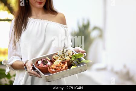 Woman holding a variety of Spanish seafood with grilled spicy prawns and seasoned clams in a metal oven tray outdoors in sunlight with copy space Stock Photo