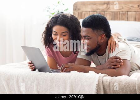 Relaxed african man and woman resting at bedroom, using laptop Stock Photo