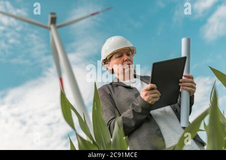 Female engineer with tablet computer on modern wind turbine farm during maintenance project planning Stock Photo