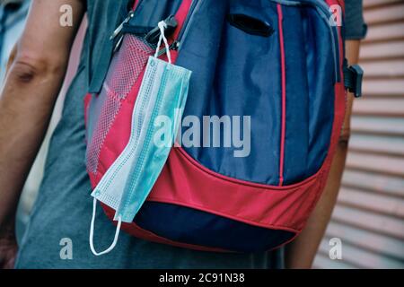 closeup of a young man on the street, in casual wear, carrying a backpack with a surgical mask hanging from it Stock Photo