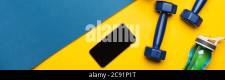 top view of blue fitness mat with dumbbells, smartphone and sports bottle on yellow background, panoramic shot Stock Photo