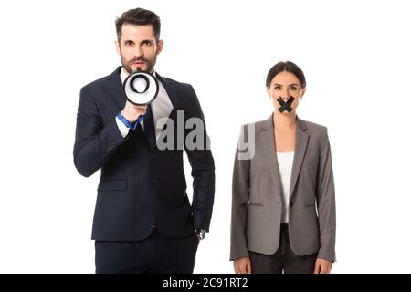 bearded businessman standing with hand in pocket and holding megaphone near businesswoman with duct tape on mouth isolated on white Stock Photo