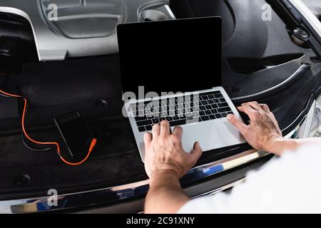 Cropped view of auto mechanic using laptop on car near wires and multimeter at service station Stock Photo