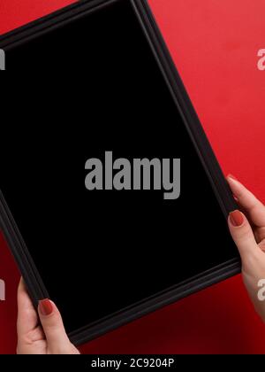 Top view of female hands holding a black empty frame in a red background with space for text Stock Photo