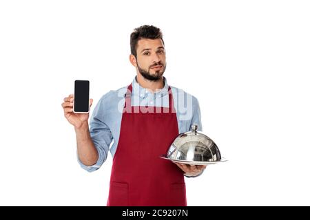 Handsome waiter holding smartphone and tray with cloche isolated on white Stock Photo