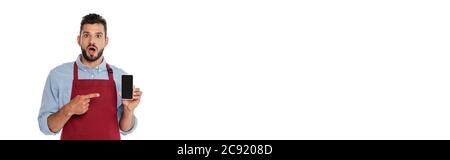 Panoramic shot of shocked waiter pointing with finger at smartphone with blank screen isolated on white Stock Photo
