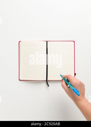 Top view of an open blank red notebook in the center, and a female hand holding a blue pen in white background, with space for text Stock Photo