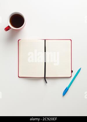Top view of an open blank red notebook in the center, a red cup of coffee and a blue pen in white background, with space for text Stock Photo
