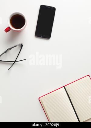 Top view of an open red notebook, a red cup of coffee, a cell phone and glasses in white background, with space for text in the center Stock Photo