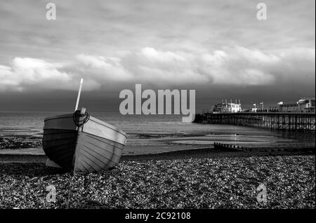 Worthing seafront West Sussex England UK - Red & blue fishing boat on the beach with Worthing Pier behind at dusk Stock Photo