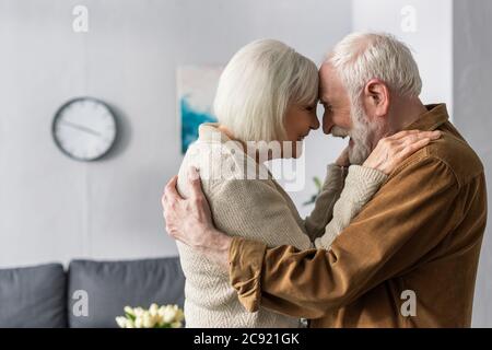 side view of happy senior couple embracing and laughing while standing face to face Stock Photo