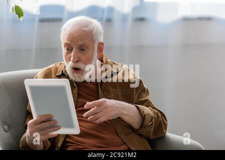 shocked senior man pointing with finger while using digital tablet Stock Photo