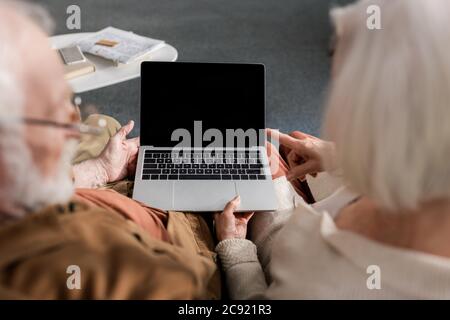 selective focus of senior couple using laptop with blank screen, overhead view Stock Photo