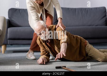 senior man lying on floor and trying to get walking stick while wife helping him Stock Photo