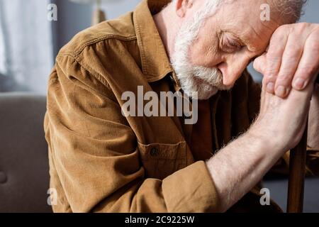 senior, depressed man sitting with bowed head while leaning on walking stick Stock Photo
