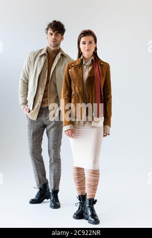 full length view of young, stylish couple in trendy autumn clothes posing on grey Stock Photo