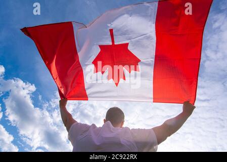 Man holding The National Flag of Canada against blue sky Stock Photo