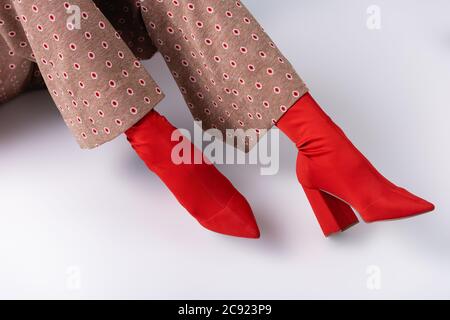 cropped view of woman in fashionable trousers and red boots sitting on white floor Stock Photo