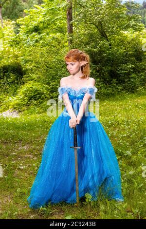 Girl with elegant dress and red hair leans on a sword Stock Photo