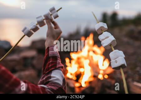 cropped view of couple holding sticks with puffy marshmallows near bonfire Stock Photo