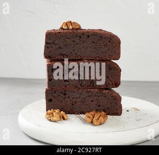 stack of baked pieces of brownie chocolate cake with nuts on a wooden board, delicious dessert Stock Photo
