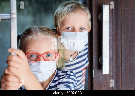 Little children looking unhappy and depressed after staying at home due banned street activity. Kids wearing medical face masks go out for  walk Stock Photo