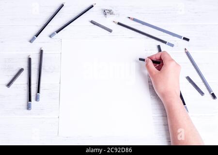 Mock up for a drawing. Hands drawing by compressed charcoal. A few pencils and black compressed charcoal. View from above. Stock Photo
